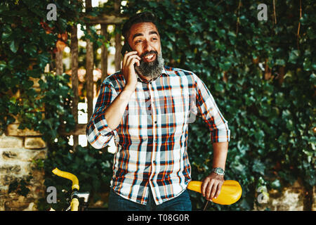 Un beau jeune homme va à la ville avec son vélo, debout à côté d'elle, l'attente de quelqu'un et parler sur le smartphone. Banque D'Images