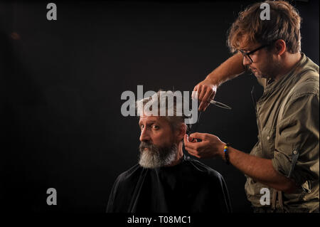 Coiffure Coupe Senior citizen avec une barbe sur fond sombre dans le studio Banque D'Images