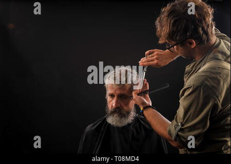 Coiffure Coupe Senior citizen avec une barbe sur fond sombre dans le studio Banque D'Images