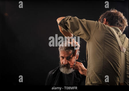 Coiffure Coupe Senior citizen avec une barbe sur fond sombre dans le studio Banque D'Images