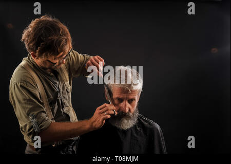 Coiffure Coupe Senior citizen avec une barbe sur fond sombre dans le studio Banque D'Images