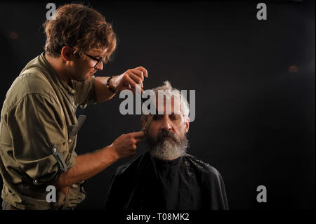 Coiffure Coupe Senior citizen avec une barbe sur fond sombre dans le studio Banque D'Images