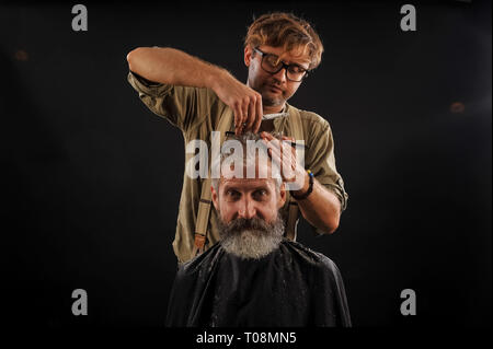 Coiffure Coupe Senior citizen avec une barbe sur fond sombre dans le studio Banque D'Images