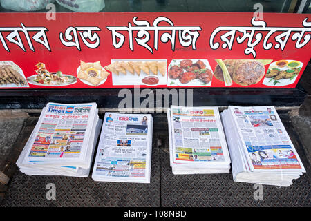 Des piles de journaux gratuits Begali entassés à l'extérieur d'un restaurant au Bangladesh sur 74e Rue à Jackson Heights, Queens, New York City Banque D'Images