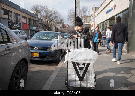 Une femme plus âgée dans un Knit hat poussant un caddie sur 82nd Street à Jackson Heights, Queens, NYC près du train no 7 . Banque D'Images