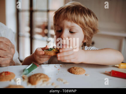 Un petit bébé garçon assis à la table, de décoration et de manger des gâteaux à la maison. Banque D'Images