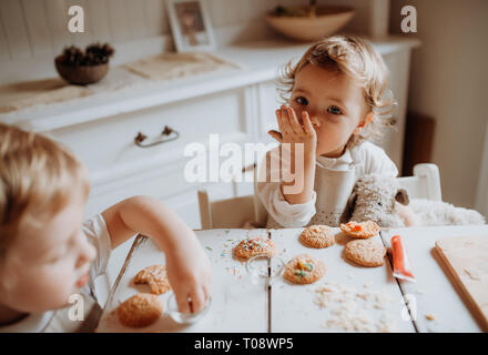 Deux petits tout-petits enfants assis à la table, de décoration et de manger des gâteaux à la maison. Banque D'Images