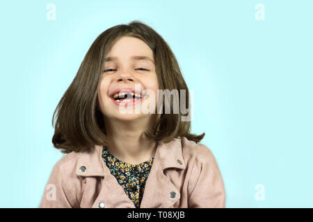 Petite fille aux dents manquantes rire avec fond bleu Banque D'Images