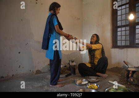 Femme assise rurale dans la cuisine la cuisine sur bois avec des ustensiles et des légumes sur le sol et sandwichs de donner à son école aller fille. Banque D'Images