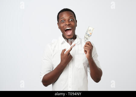 Les jeunes riches african american man in shirt holding one hundred dollar avec surprise Banque D'Images