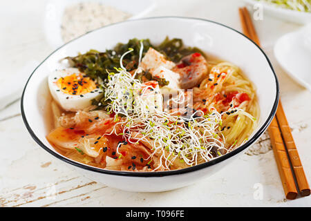 Le miso Ramen nouilles asiatiques au chou kimchi, algues, champignons, oeuf et fromage de tofu dans la bol sur une table en bois blanc. La cuisine coréenne. Banque D'Images