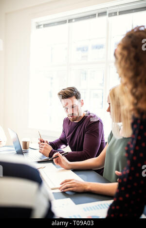 Groupe de jeunes créateurs discussing paperwork, tandis qu'assis autour d'une table de conférence dans un bureau Banque D'Images