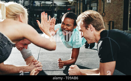 Mettre en place deux jeunes femmes en train de rire et de sportswear fiving haut, tandis qu'avec les amis de planches sur le sol d'une salle de sport Banque D'Images