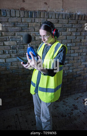 Un arpenteur de l'environnement femmes tests pour le son et le bruit durant une enquête sur un chantier à l'aide d'équipements spécialisés. Banque D'Images