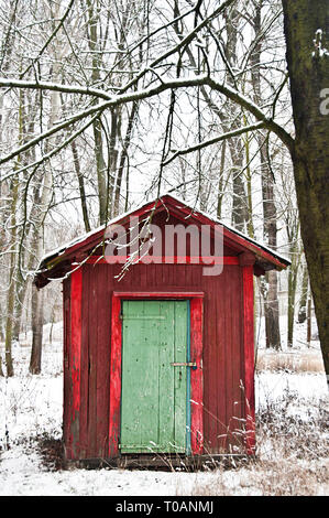 Rouge ou hutte avec porte verte dans la forêt au cours de la neige en hiver Banque D'Images