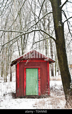 Rouge ou hutte avec porte verte dans la forêt au cours de la neige en hiver Banque D'Images