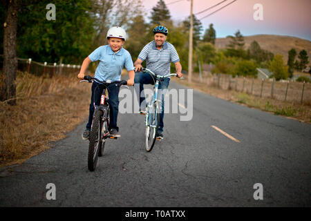 Portrait of a happy father and son riding bikes le long d'une route de campagne. Banque D'Images