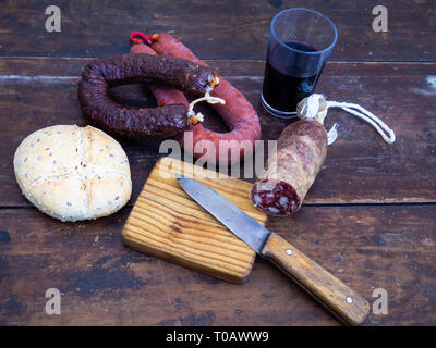 Saucisses de porc ibérique sur une vieille planche en bois avec un morceau de fromage de brebis, un ancien couteau et un verre de vin rouge Banque D'Images