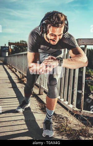 Les jeunes sportifs avec des écouteurs démarre le chronomètre avant l'entraînement sur le pont. Il se prépare pour le jogging. Banque D'Images