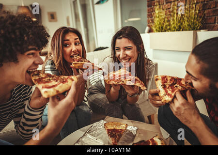 Amis est excité à la maison assis sur un canapé. Amener leurs amis à pizza manger ensemble. Elles ont un grand week-end à Nice à l'intérieur de l'entreprise. Banque D'Images