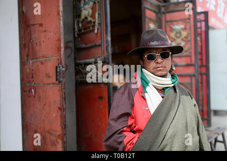 Le port de lunettes de soleil homme tibétain debout près de la fenêtre, Sichuan, Chine Banque D'Images