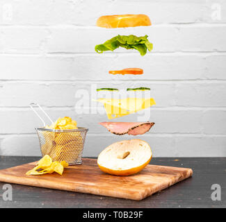 Sandwich Bagel Lévitation flottant relevant des ingrédients. Produits frais et délicieux sandwich magique. Blanc rustique / mur de brique rouge. Chips / croustilles Banque D'Images