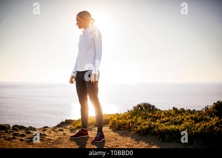 Jeune femme prend une pause de son jog lever du soleil le long des falaises pour admirer la vue sur l'océan. Banque D'Images