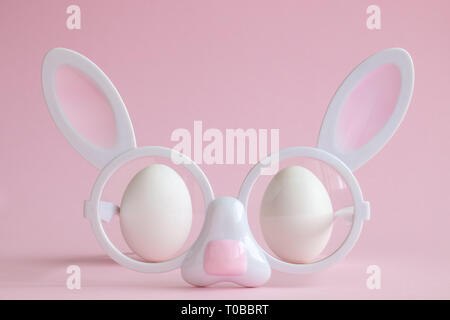 Bunny en forme de visage Lunettes avec deux œufs blancs sur fond rose pastel créative concept minimal de Pâques. Banque D'Images