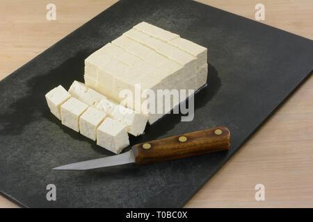 Bloc de tofu extra ferme coupé en cubes sur une planche à découper avec couteau de cuisine à préparer pour l'ajout d'ingrédient comme repas dans la cuisine Banque D'Images