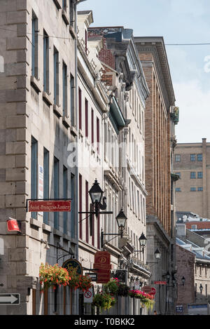 Montréal, Québec, Canada. Paniers de fleurs suspendus et enseignes de boutiques le long de la rue Saint-Paul Ouest à Saint François-Xavier, dans le Vieux Montréal. Banque D'Images