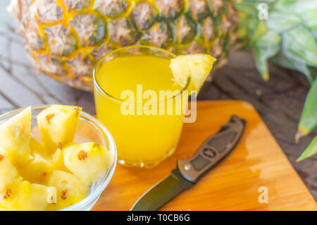 Vue latérale d'ananas entier conservé sur une table en bois en plus d'un verre rempli de jus d'ananas et un bol en verre avec des tranches d'ananas et un couteau kep Banque D'Images