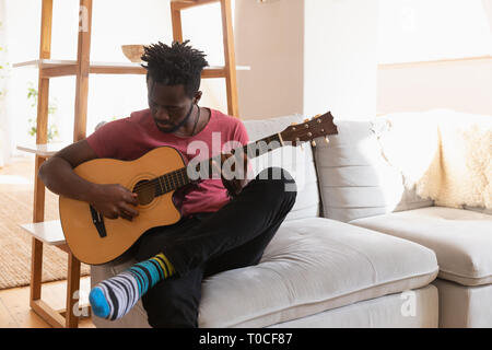 L'homme qui joue de la guitare tout en restant assis à la maison dans une pièce à vivre Banque D'Images
