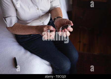 Active senior woman glucomètre avec contrôle de niveau de sucre dans le sang sur le lit dans la chambre à la maison Banque D'Images
