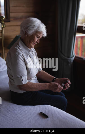 Active senior woman glucomètre avec contrôle de niveau de sucre dans le sang sur le lit dans la chambre à la maison Banque D'Images