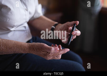 Active senior woman glucomètre avec contrôle de niveau de sucre dans le sang sur le lit dans la chambre à la maison Banque D'Images