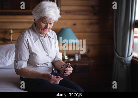 Active senior woman glucomètre avec contrôle de niveau de sucre dans le sang sur le lit dans la chambre à la maison Banque D'Images