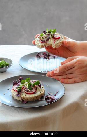 Le tableau mis en place avec des sandwichs avec du fromage, radis et pousses (pousses) et femme mains tenant un sandwich Banque D'Images