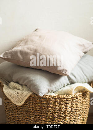 Panier en osier blanc avec une couverture en tricot doux et coussins gris contre un mur blanc. copy space Banque D'Images