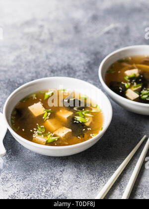 La soupe miso japonaise aux pleurotes dans un bol blanc avec une cuillère et baguettes blanches sur fond gris. Banque D'Images