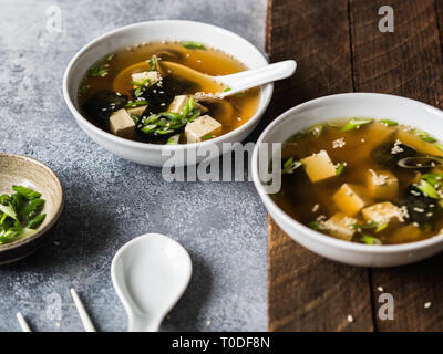 La soupe miso japonaise aux pleurotes dans un jeu de boules avec une cuillère et baguettes blanches sur un fond gris et de bois. Banque D'Images