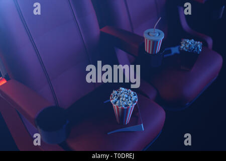 Illustration 3D avec lunettes 3D, pop-corn, tasse avec une boisson. Concept de cinéma avec lumière bleue. Chaises rouges dans la salle de cinéma. Banque D'Images