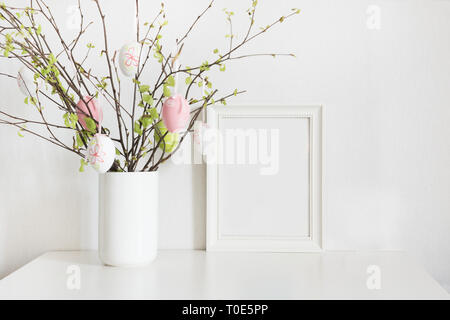 Easter home intérieur. Décoration saisonnière. Vase avec des branches d'arbres de bouleau avec les oeufs de Pâques et le châssis pour le texte et les désirs contre un mur blanc backgroun Banque D'Images