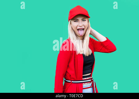 Portrait de funny crazy beautiful blonde jeune femme style hippie en blouse rouge et le chapeau, debout, de la langue et à la caméra à l'intérieur studio sho.