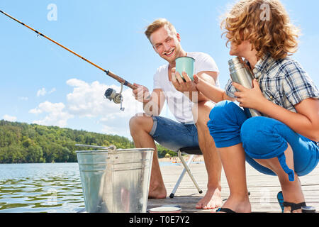 Le père et le fils de boire une tasse de café ensemble alors que la pêche sur le lac Banque D'Images