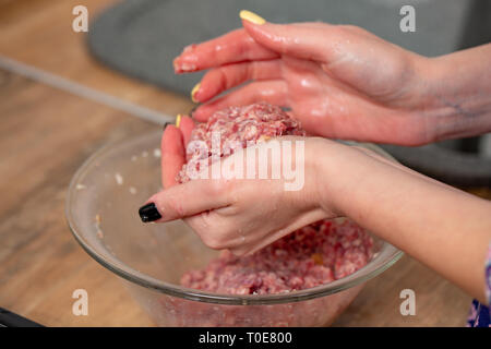 La viande hachée crue dans les mains de femme svelte. La cuisine de fille sur escalopes cuisine moderne Banque D'Images