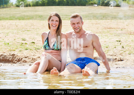 Heureux couple assis sur la plage par la mer et garder leurs pieds cool les vacances d'été Banque D'Images