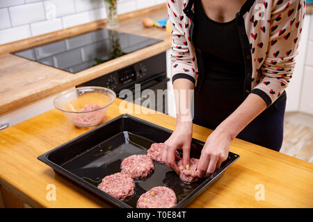 Jeune femme la cuisson des boulettes de viande ou les escalopes dans une cuisine moderne. Femme de la viande s'étend sur une plaque de cuisson de la viande. Banque D'Images