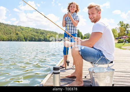 Père et fils de pêche sur une jetée au bord du lac ensemble sur le week-end en été Banque D'Images