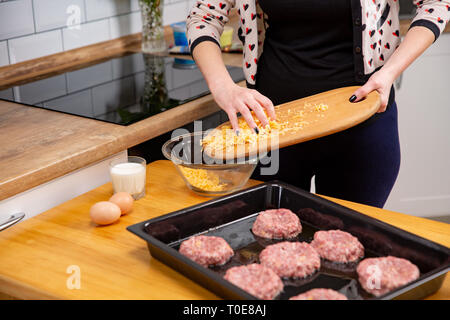 Verser la main féminine avec du fromage râpé de découper à la plaque. Processus de cuisson les escalopes ou boulettes de viande. La cuisine maison moderne sur kithen Banque D'Images