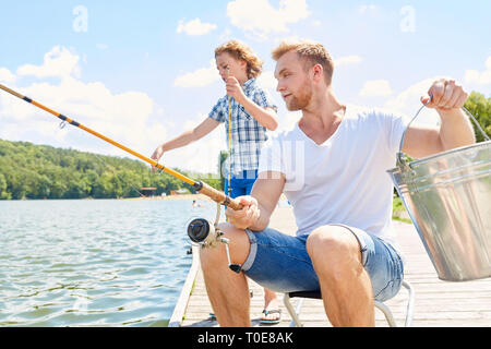 Père et fils au bord du lac sont la pêche ensemble sur une jetée en été, pendant les vacances Banque D'Images